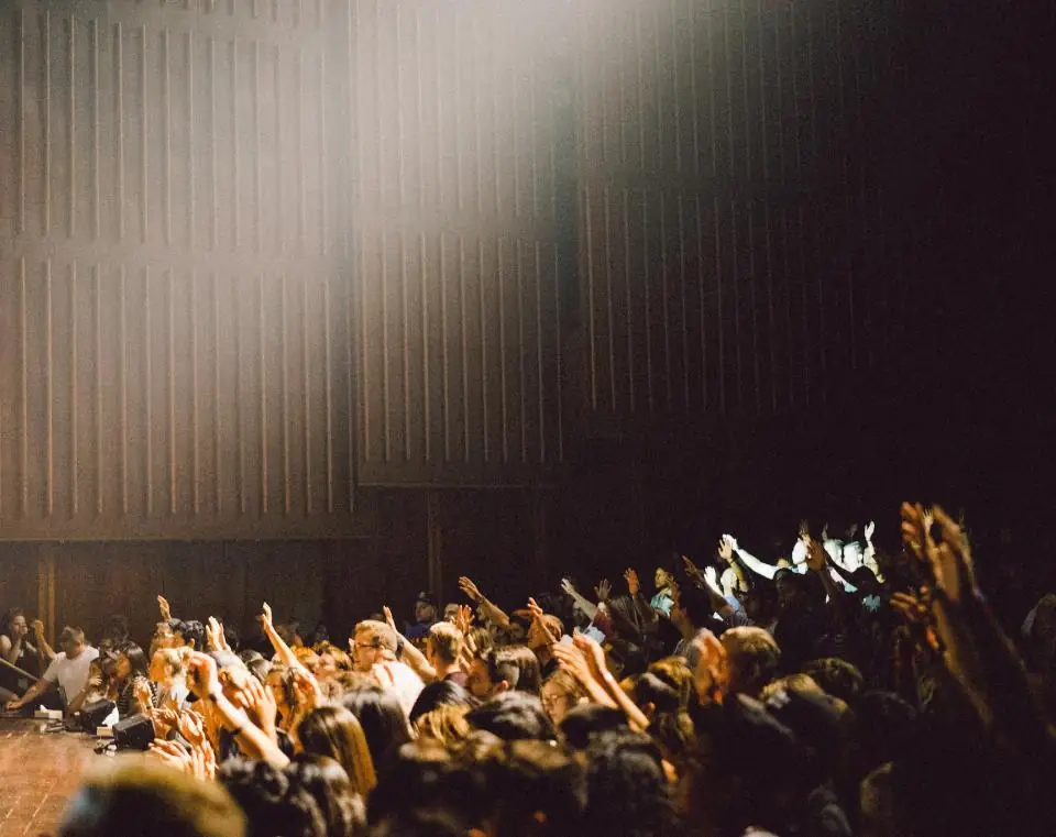 A congregation with hands raised in worship under warm light